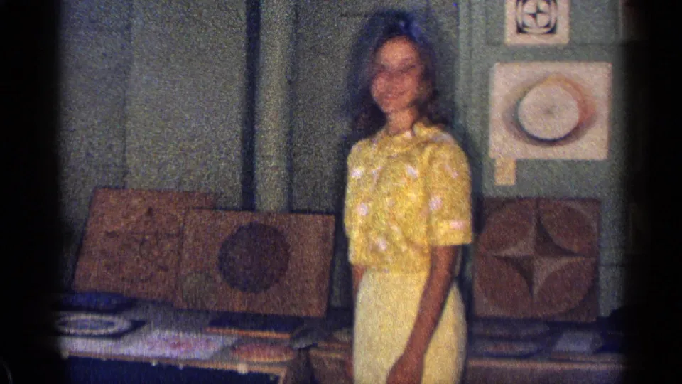 Young woman in a yellow patterned dress stands before a 1963 Texas wall display of geometric art and drawings.