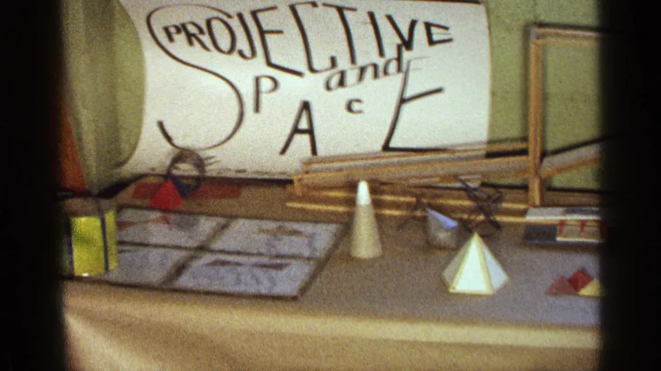 Texas 1963 home-movie frame of a school science fair table labeled projective space, with cones, pyramids, rods, and papers.