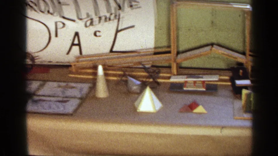 Texas 1963 8mm frame showing cones, pyramids, folded paper shapes, rods, and display papers beneath a projective space sign.