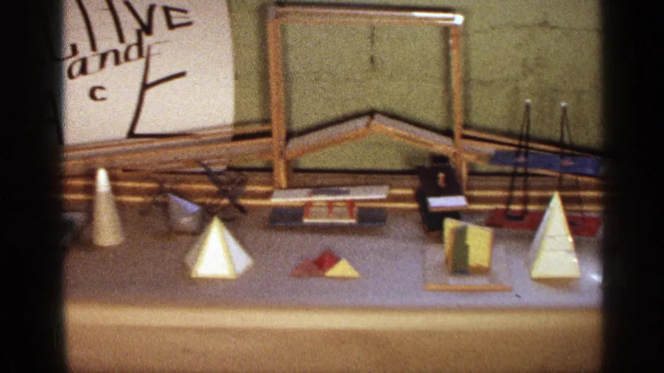 Texas 1963 home-movie frame of a student display table with geometric models, rods, a small box, and a partial projective space sign.