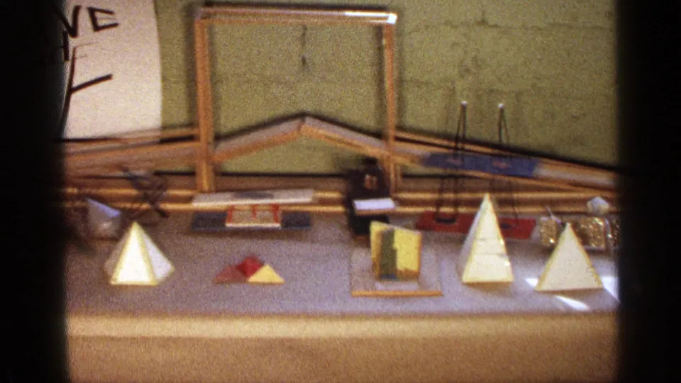1963 Texas 8mm frame showing wooden pyramids, prisms, and a larger frame structure on a light tabletop.
