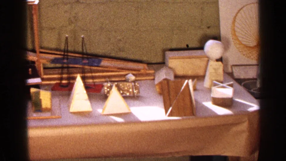 1963 Texas home-movie frame showing pyramids, a standing wooden panel, a small cube form, and a board with circular line drawing.