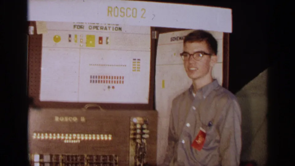In 1963 Texas footage, a young man in glasses stands next to a Rosco II console beneath a labeled operation diagram.