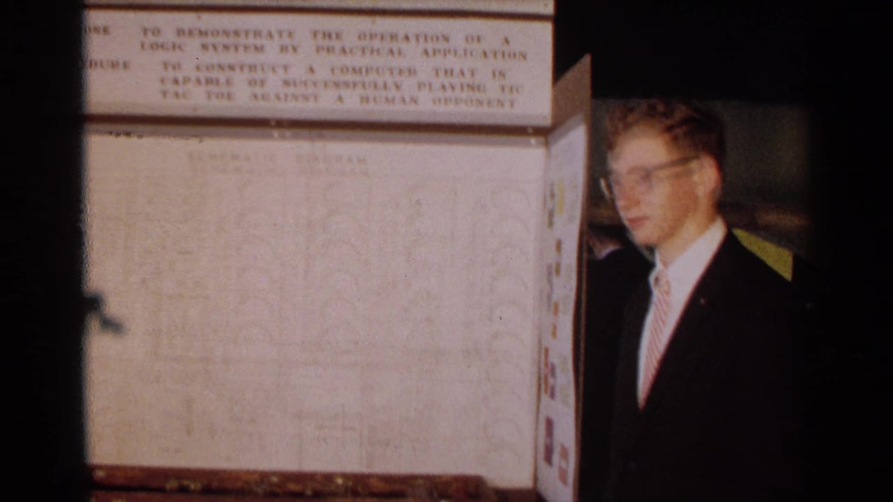 The student presenter stands beside the schematic section of a 1963 Texas logic systems science fair exhibit.
