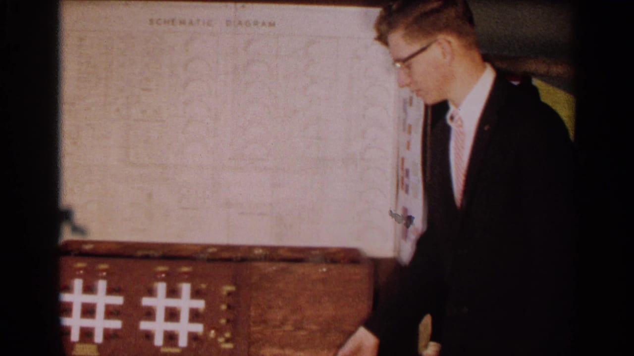 A student in a dark suit stands beside the logic systems project, with illuminated tic-tac-toe grid patterns visible on the base.