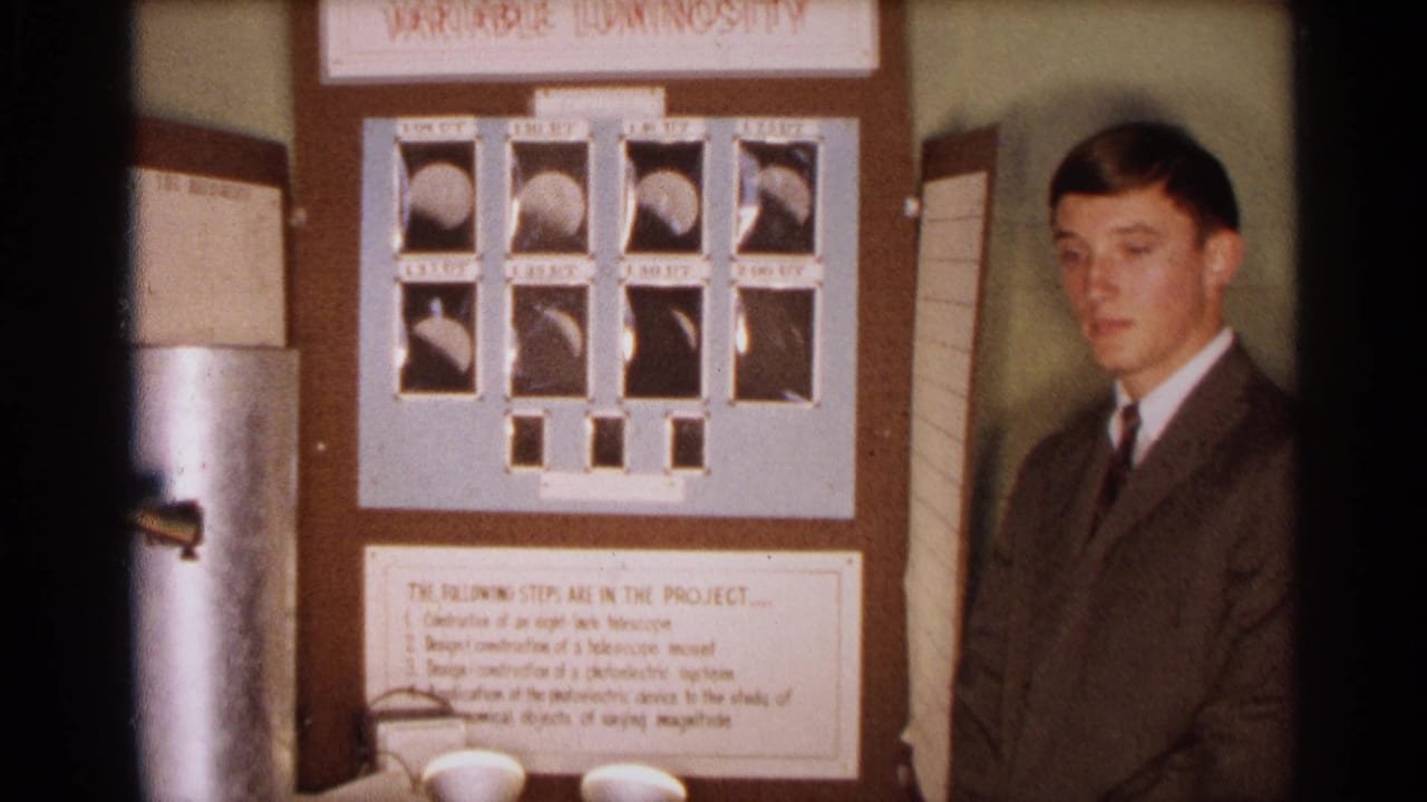 In 1963 Texas home-movie footage, a young man in a suit stands beside a Variable Luminosity school science project board.
