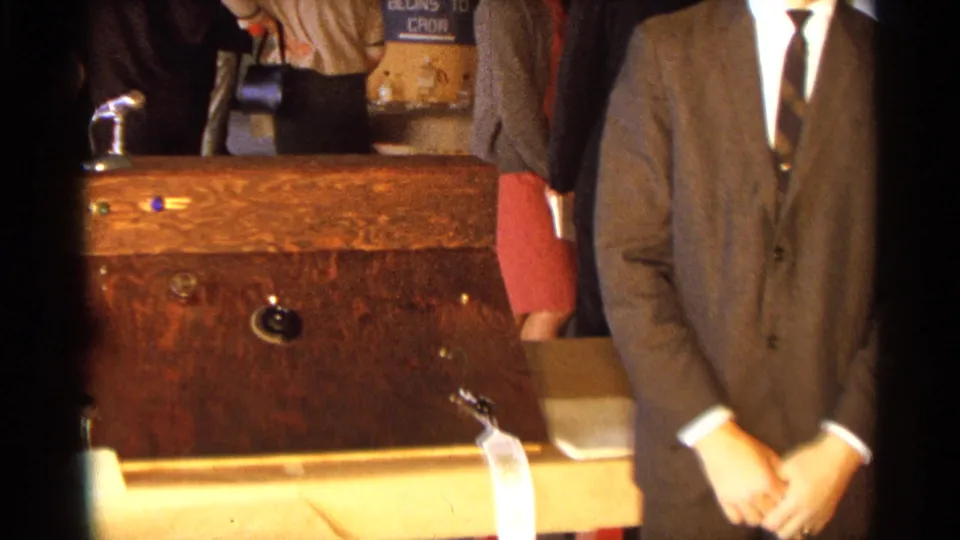 The 8mm frame centers on a wooden science project control box, with the young man partly cropped at right.
