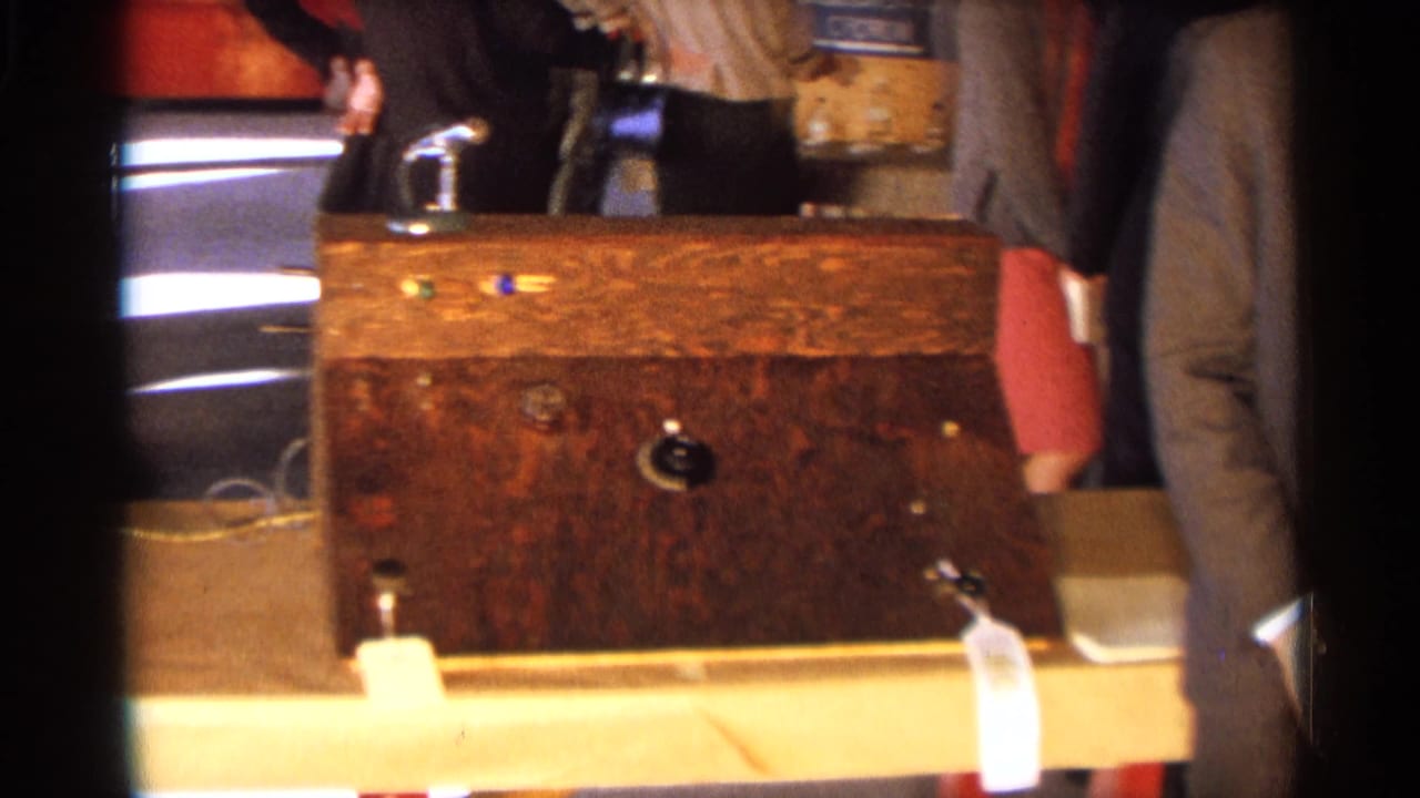 Wooden display case with a small rocket model, with adults partly visible behind it.
