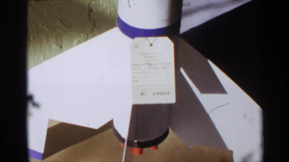 Close-up of a model rocket exhibit with a hanging tag marked No 10052, shown in 1963 Texas 8mm footage.