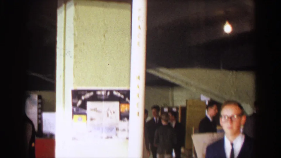 Indoor 1963 Texas science exhibition view with a model rocket, display boards, and several adults visible in the background.