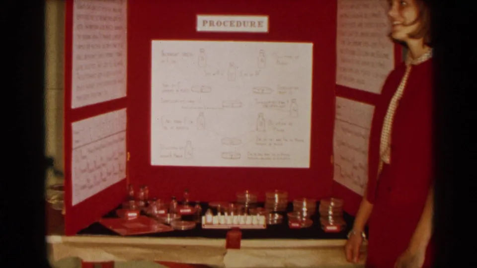 The red virus resistance display is shown with petri dishes and small lab containers arranged on the table below, while the presenter stands at right.