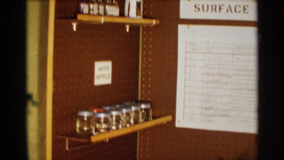 1963 Texas frame with a pegboard-mounted science display, labeled jars on shelves, and a pinned surface-water sample chart.