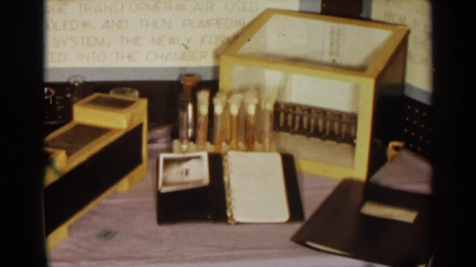 Close 1963 Texas 8mm view of the ozone project apparatus, including glass tubes, small containers, a notebook, and a box-like device.
