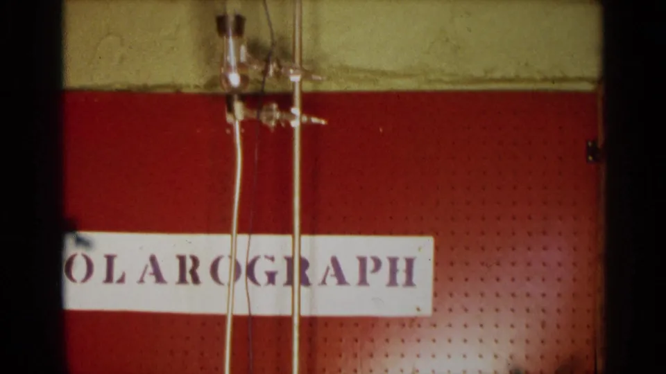 1963 Texas 8mm frame showing a red pegboard panel, vertical glass tubes, wiring, and a sign reading polarograph.