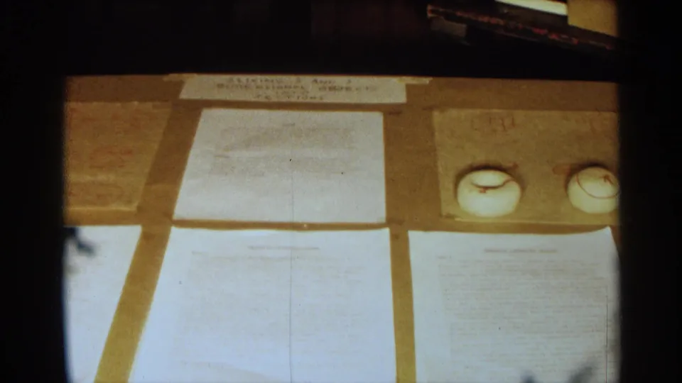 Close 1963 Texas 8mm view of typed papers and small white round objects arranged on a covered table.