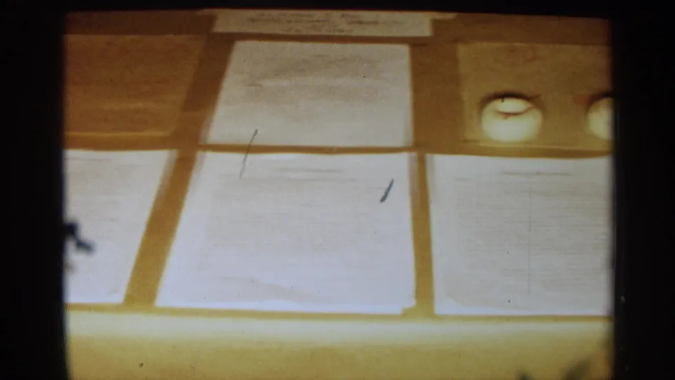 Texas 1963 8mm frame showing close-up papers on a science exhibit display, with warm exposure and soft focus.