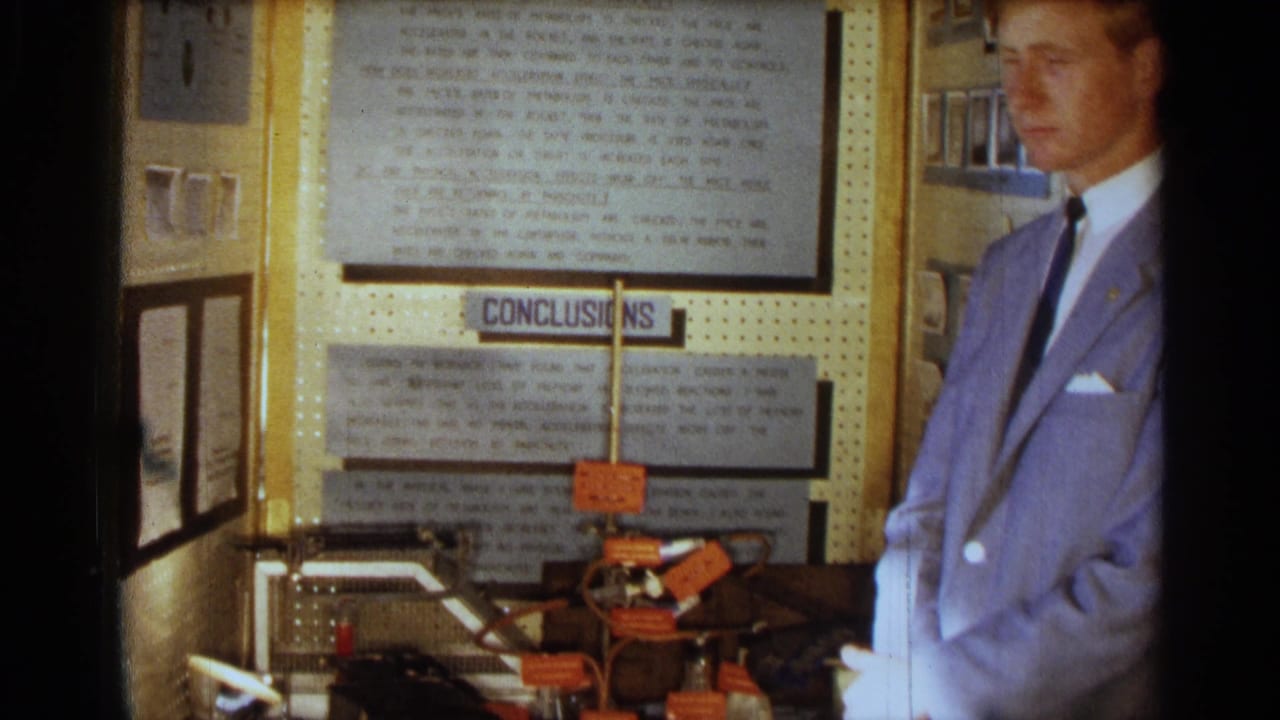 Young man stands at the right of a project display with wires and orange labels on a table.