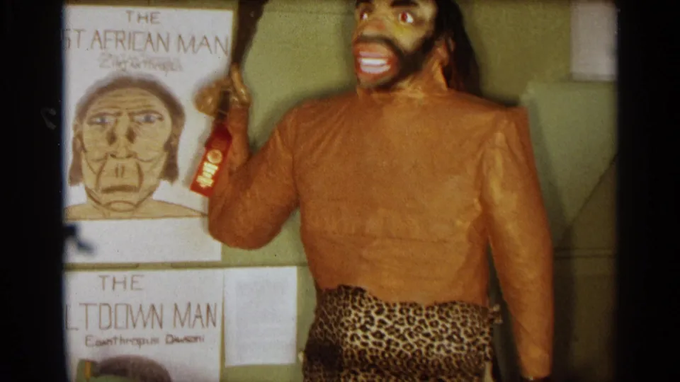 1963 Texas exhibit showing a prehistoric-style mannequin in animal-print fabric beside hand-lettered early human posters.
