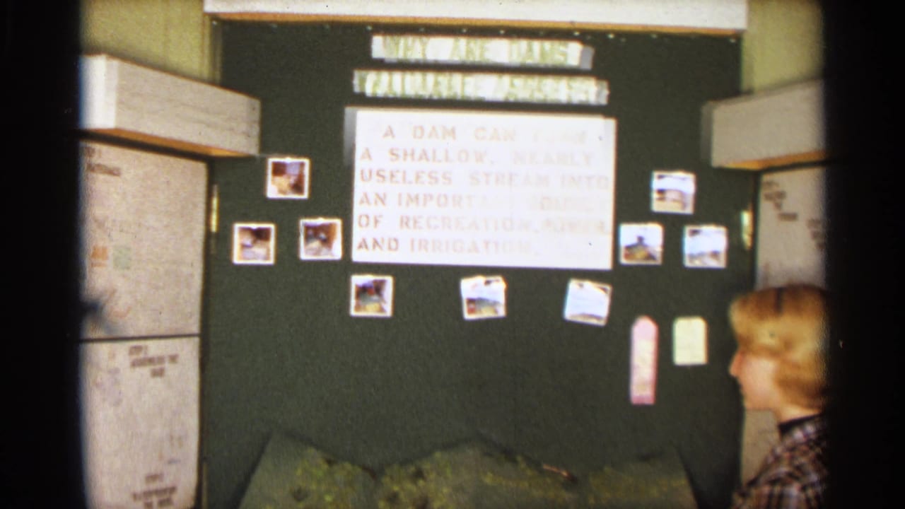 A girl passes in front of the 1963 Texas classroom display, with the dam project title and model landscape visible behind her.