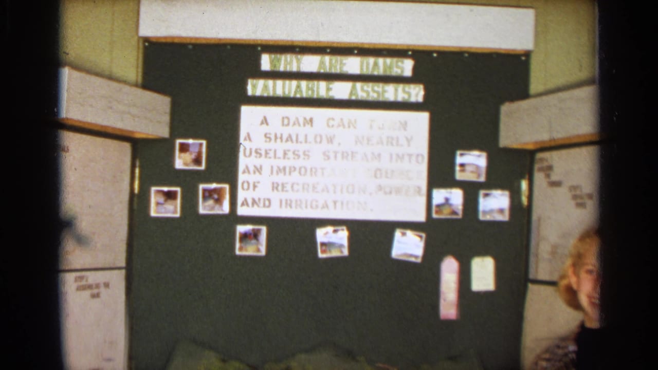 At the edge of the frame, the girl smiles beside the 1963 Texas classroom dam-project display and photo-covered bulletin board.