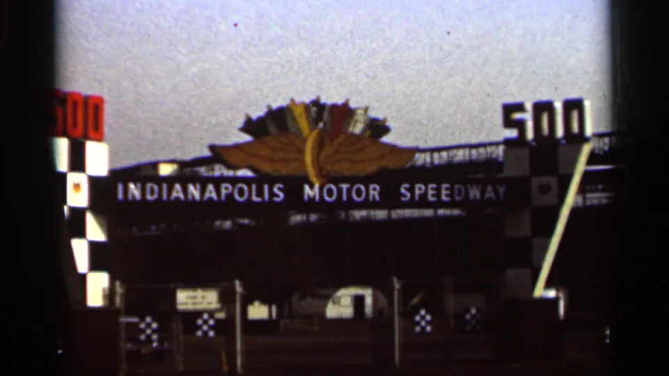 1964 8mm frame of the Indianapolis Motor Speedway entrance, with winged emblem, large 500 numerals, and checkered columns.