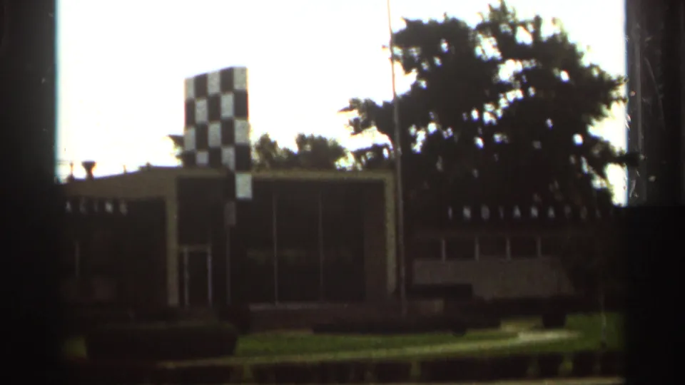 1964 Indianapolis Motor Speedway view with the checkered tower, low buildings, grass, and trees.