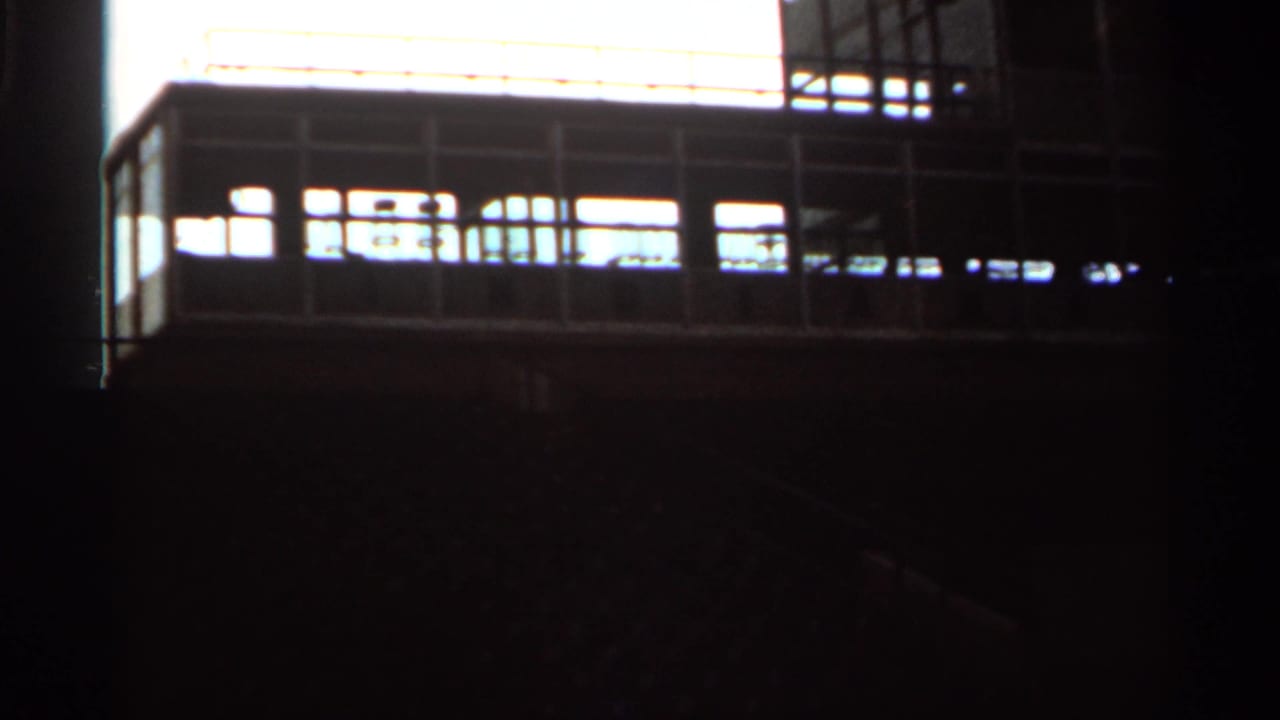 Low-angle 1964 8mm view of empty Indianapolis grandstand seating and railings in strong backlight.