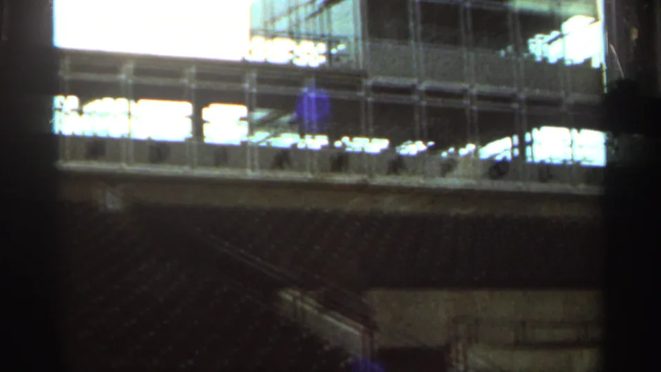 1964 Indianapolis Motor Speedway frame showing empty seating, railings, and a glass-fronted trackside structure.