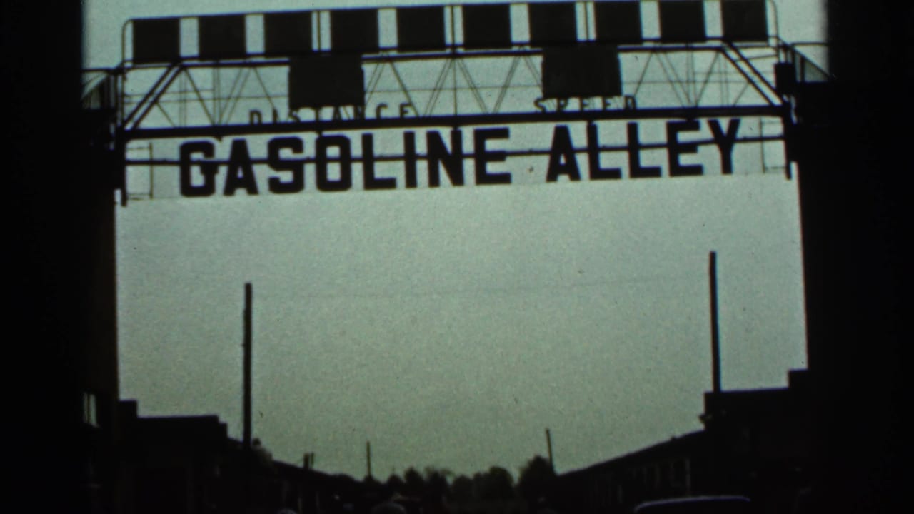 1964 Indianapolis home-movie frame showing a large Gasoline Alley sign over dark street silhouettes and a hazy sky.
