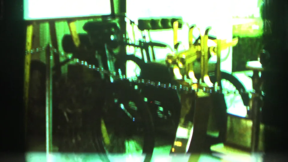Green-cast 1964 home-movie frame showing a bright display area with dark mechanical shapes and reflective window light.