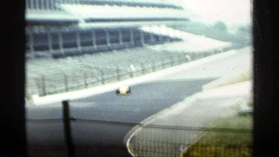 1964 Indianapolis racetrack footage shows a yellow open-wheel race car rounding a curve with fencing and empty stands nearby.
