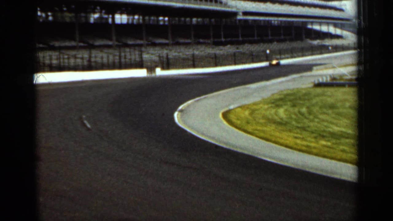 Small race car enters the bend near the outer wall of an empty speedway.