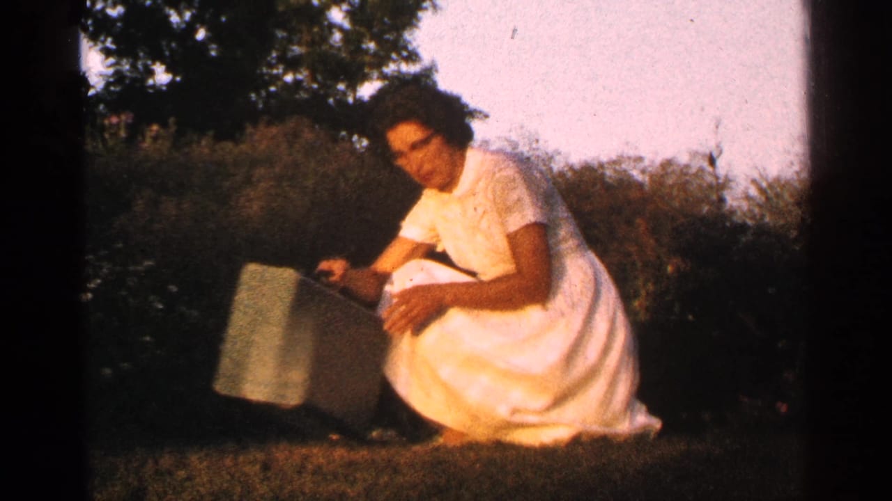 Woman in a white dress kneeling on grass beside a green case.