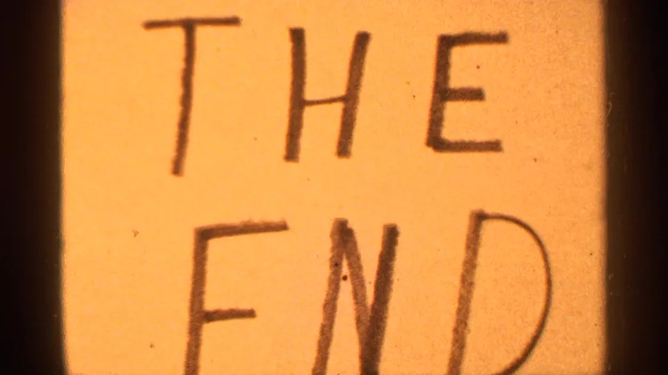 Close 8mm frame of a handmade "THE END" sign, filling most of the view with warm faded color and visible film grain.