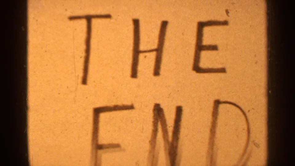 The final frame shows the handwritten "THE END" card in close-up, with soft focus, dust specks, and 8mm frame edges visible.