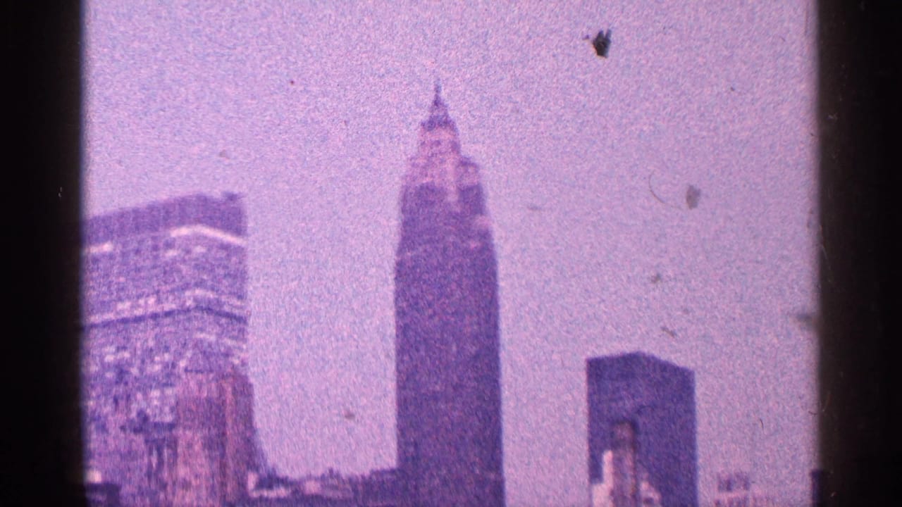 1964 8mm view of New York City skyline with the Empire State Building rising through a purple-blue haze.