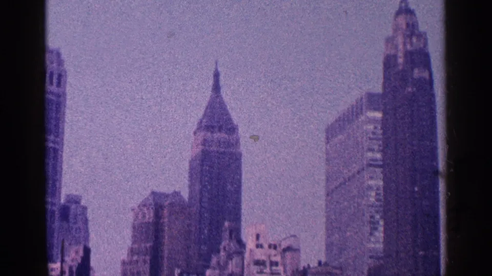 1964 8mm skyline frame showing New York City towers in soft focus with visible grain and muted color.