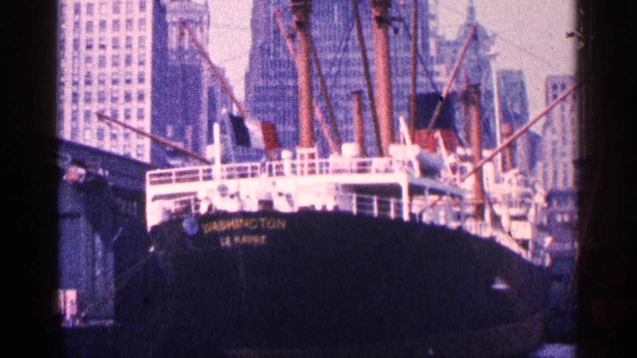 1964 New York harbor view of the SS Washington docked before tall city buildings in faded 8mm color.