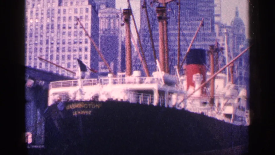 The SS Washington remains in frame with its dark hull, white decks, masts, and Manhattan towers behind it.