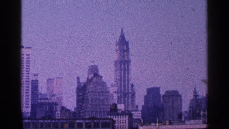 1964 home-movie view of Manhattan buildings with the Empire State Building visible through soft, blue-purple film color.