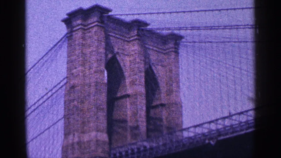 Close 1964 8mm view of the Brooklyn Bridge tower with masonry piers, arches, and diagonal suspension cables.