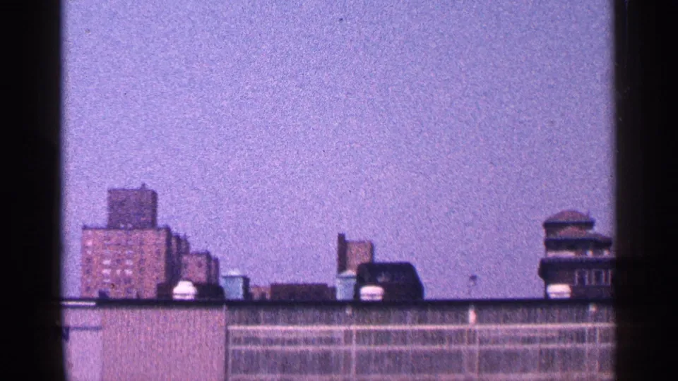 1964 New York City rooftop view with low apartment buildings, water tanks, and distant vertical structures.