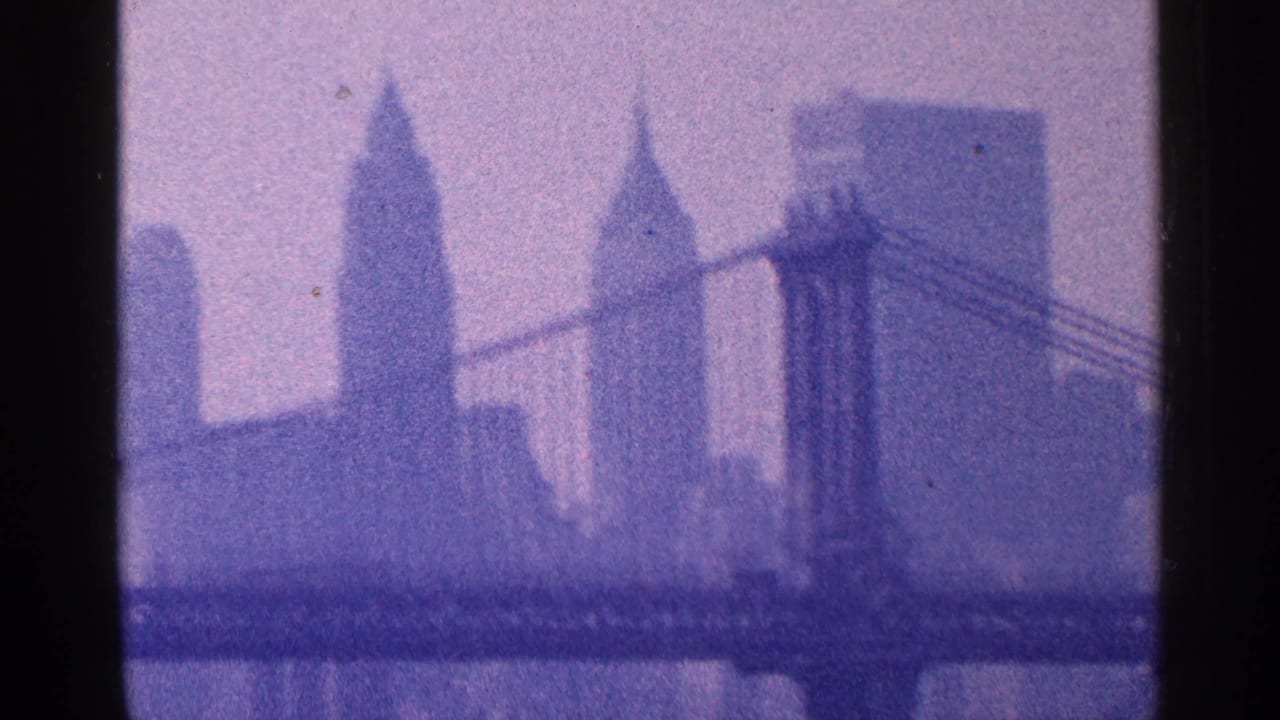 1964 New York City frame with a suspension bridge, the Empire State Building, and other Manhattan towers seen through haze.