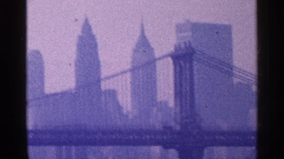 1964 New York City frame with a suspension bridge, the Empire State Building, and other Manhattan towers seen through haze.
