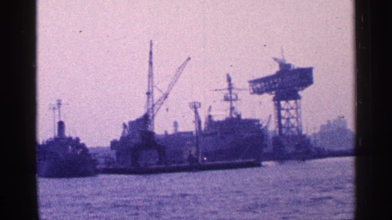 Distant harbor view with industrial ships, cranes, and water framed by dark film edges.