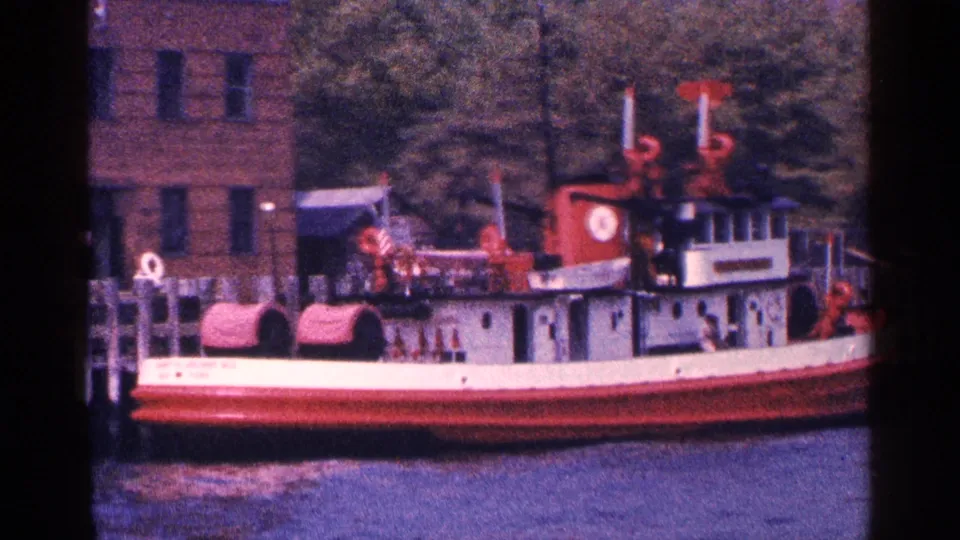 Side view of a red-and-white tugboat moored along the New York City waterfront, shot on 8mm film in 1964.