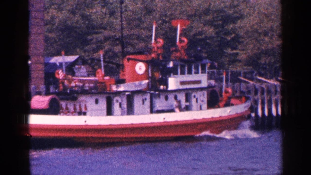 Red and white tugboat passing along a waterfront pier.