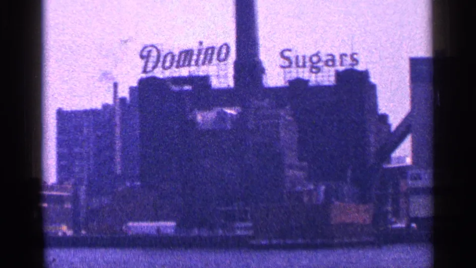 Blue-tinted 8mm frame of the Domino Sugars factory signage along the New York City waterfront in 1964.