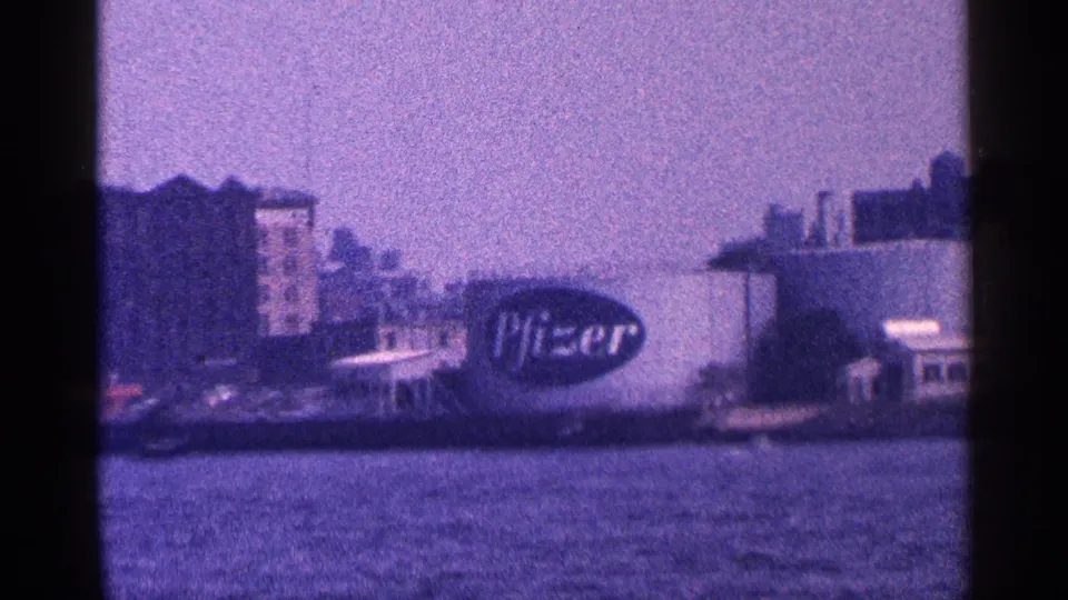 1964 New York City waterfront view from a boat, with a large Pfizer sign visible among shoreline buildings.