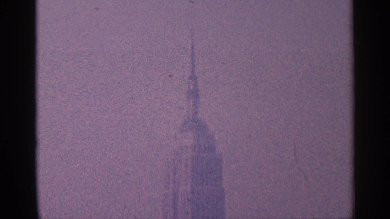 Distant New York City skyscraper spire, likely the Empire State Building, softened by haze in 1964 8mm home-movie footage.